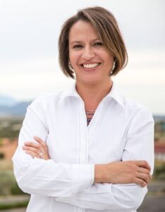 Campaign Photo of Land Commissioner Stephanie Garcia Richard in a white blouse with New Mexico Landscape behind.